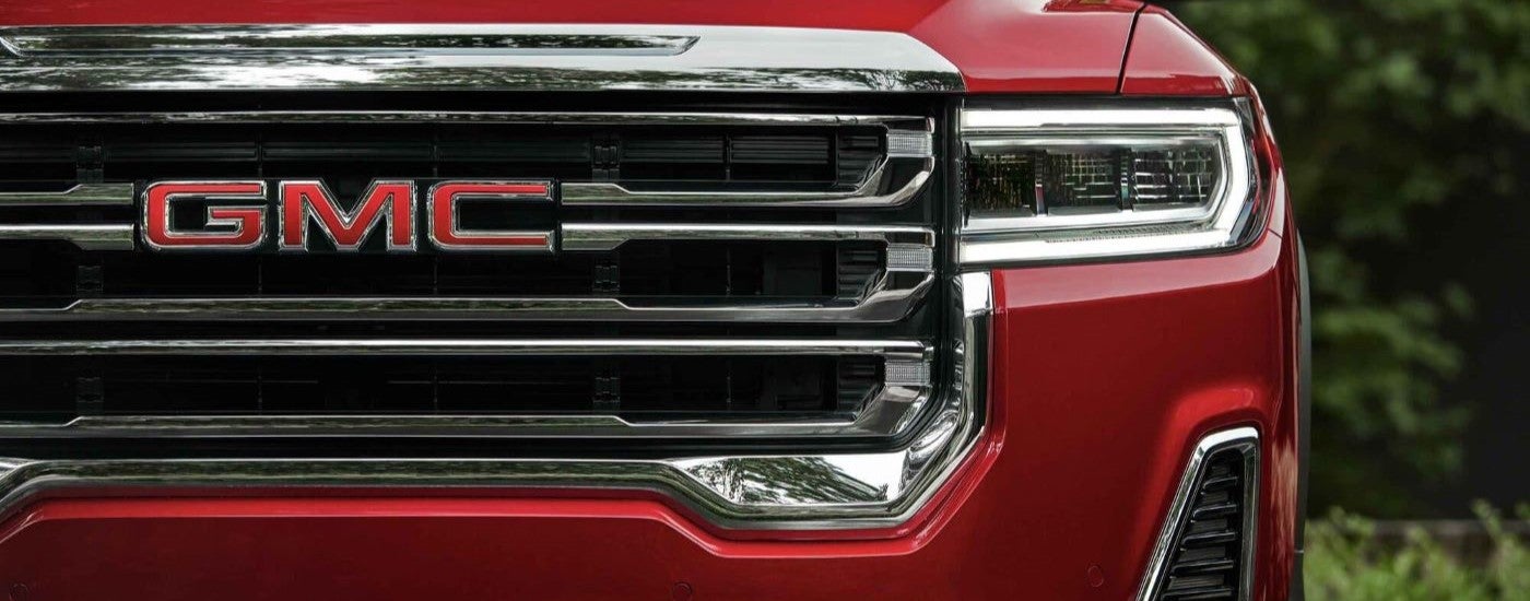 A close-up on the grille of a red 2023 GMC Acadia SLT is shown.