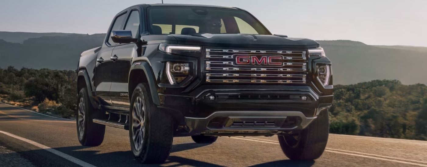 A black 2023 GMC Canyon Denali is shown driving on an open road.